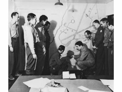 Russell pointing out the base hospital to colleagues on a wall plan of Langford Lodge.